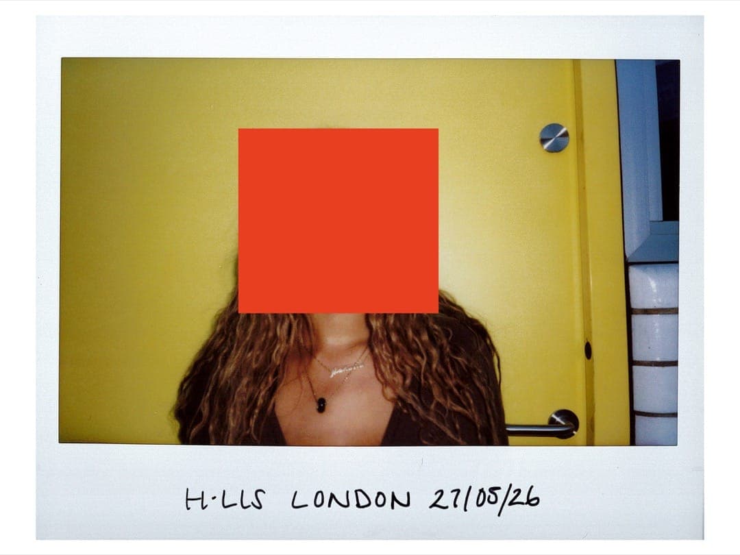 Mahalia with long curls and a name necklace by a yellow door, face behind an orange square